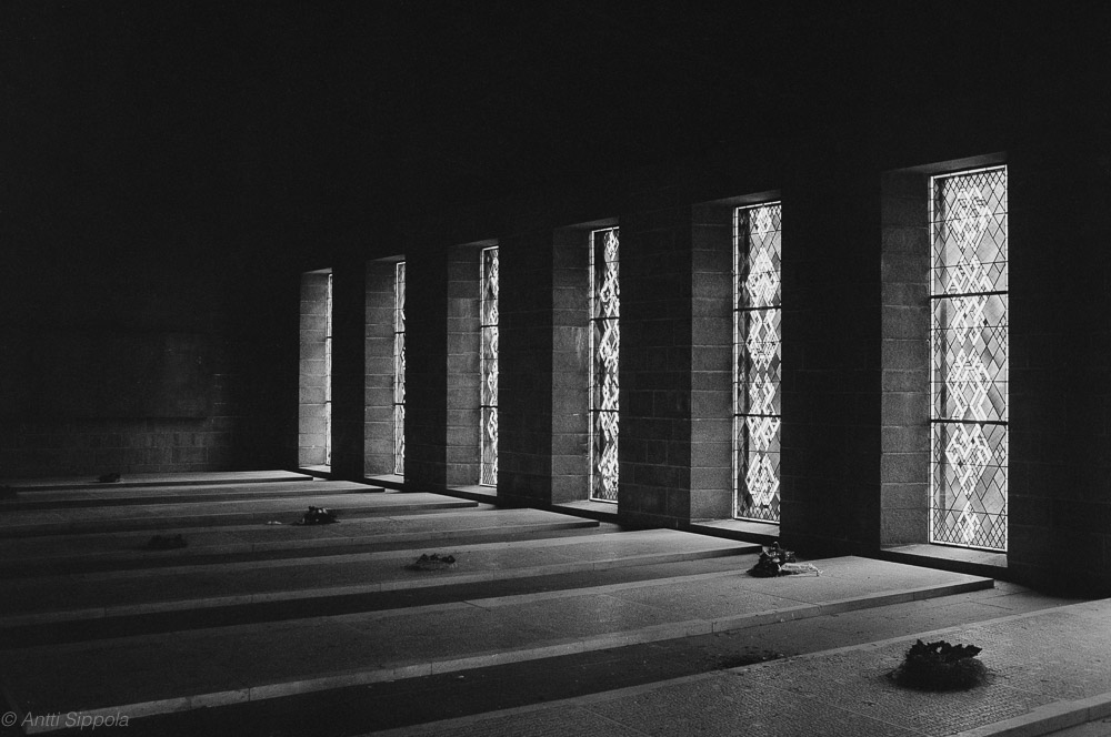 A row of tall windows illuminate the floor of a stone mausoleum.